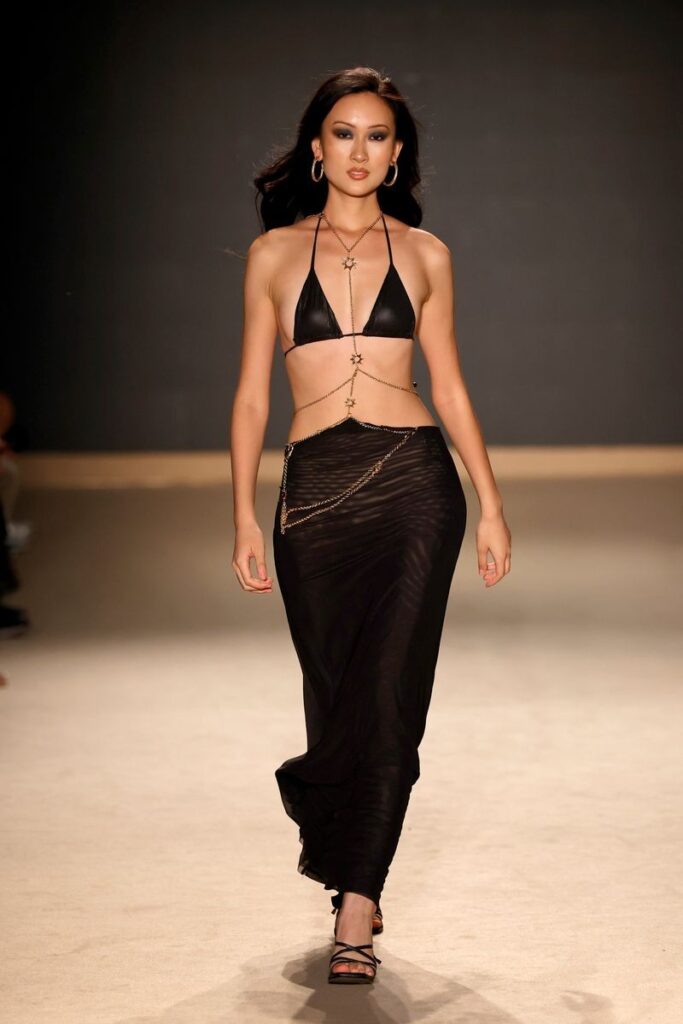 Black triangle bikini top layered with gold body chains over a long sheer black skirt, Leslie Amon runway at Miami Swim Week 2026