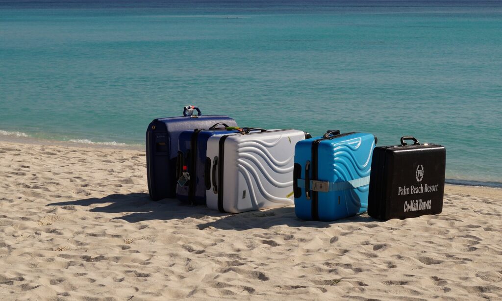 Five suitcases lined up on white sand at the water's edge, waiting for the seaplane on Madhiriguraidhoo in Lhaviyani Atoll, Maldives