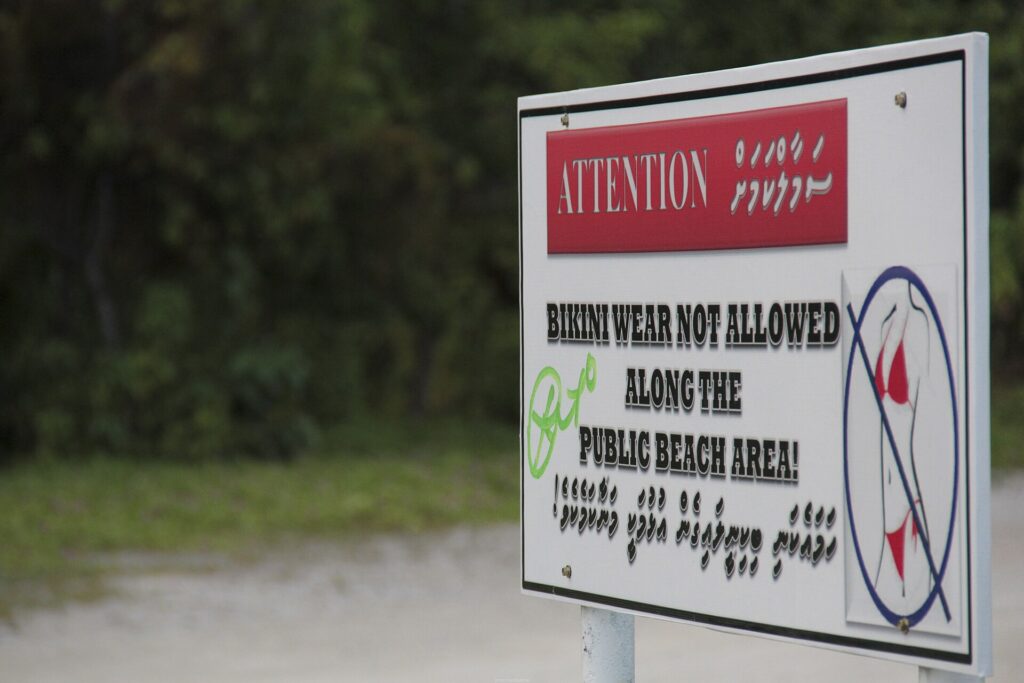 Sign on Maafushi, a local island in the Maldives, reading Attention: bikini wear not allowed along the public beach area, in English and Dhivehi