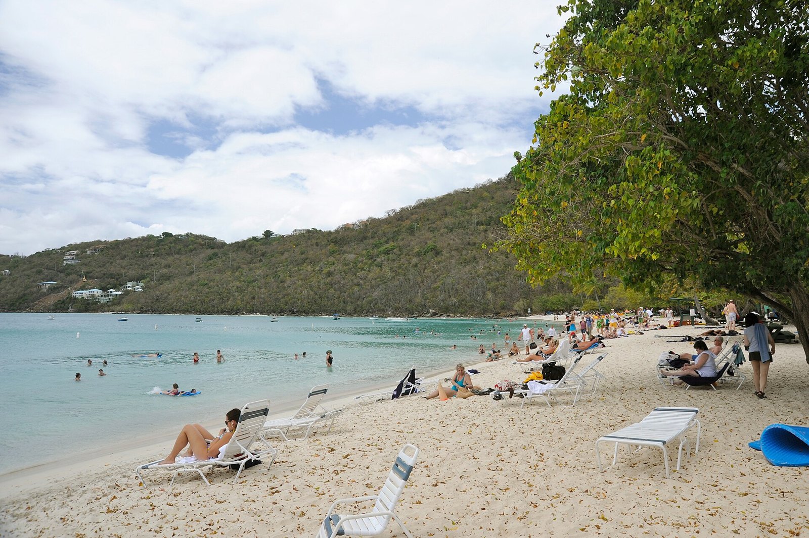Swimmers and white loungers on the sand at Magens Bay, St. Thomas, with calm turquoise water and green hills