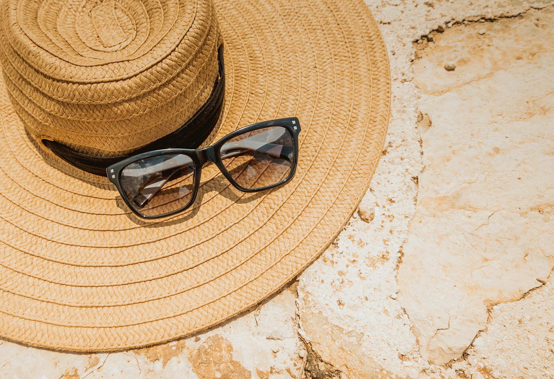 wide brim straw hat and sunglasses on sunlit stone, beach sun protection for a Tulum packing list