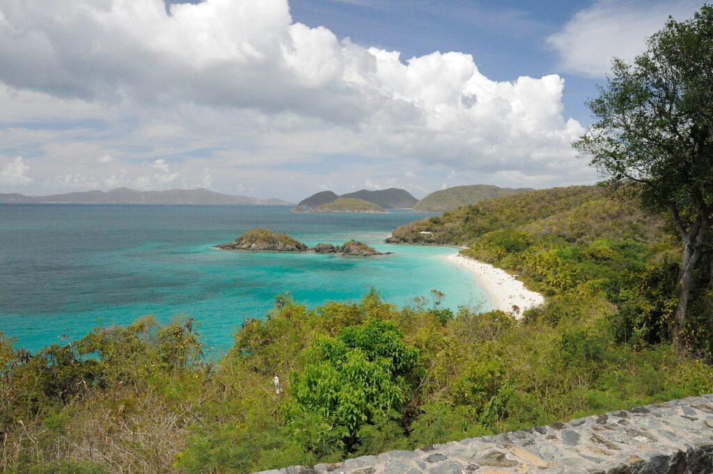 Trunk Bay on St. John in the U.S. Virgin Islands seen from the overlook: a curve of white sand, turquoise water and a small cay below green hills